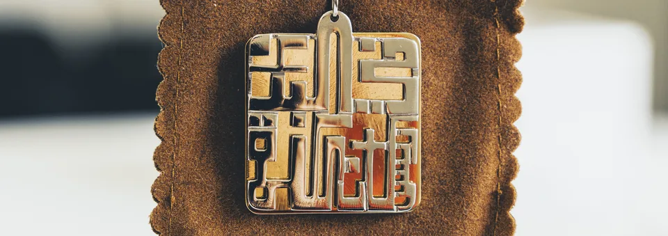 Close-up of a geometric calligraphic pendant on brown fabric