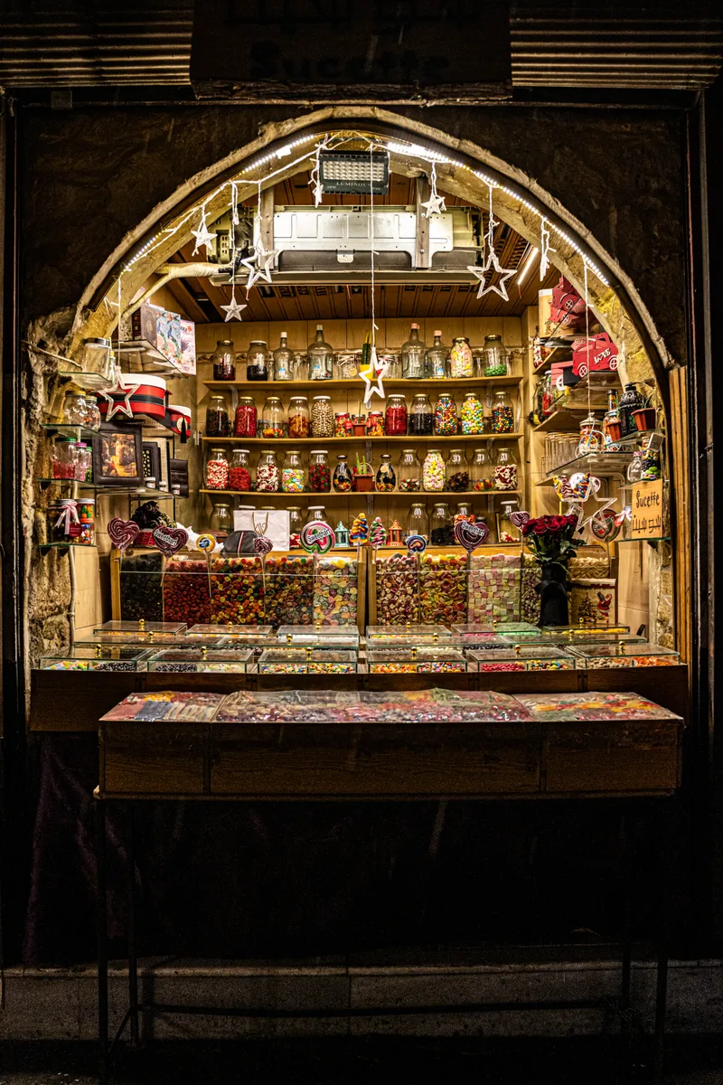 Illuminated sweet shop framed by a stone arch in Bab Sharqi